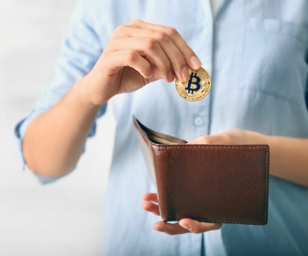 a man dropping a Bitcoin into a wallet, representing the concept of How Long Does It Take to Transfer Bitcoins Between Wallets?